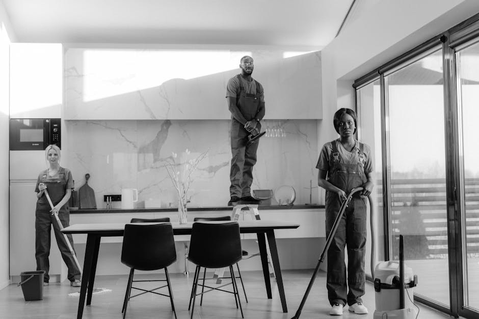 A professional cleaner from Olivia Cleaning Solutions is shown in a modern residential interior, wearing a uniform and using a long-handled squeegee to clean a large glass window or sliding door. The 